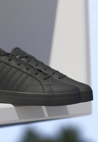 Baskets en cuir noir avec lacets et rayures reposant sur un rebord blanc sur fond gris et bleu.