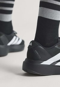 Scarpe da ginnastica Adidas Adizero Evo SL bianche e nere indossate con calzini neri con strisce orizzontali grigie e nere.