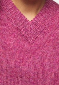V-ringad tröja i en melerad rosa stickning, med ribbat nacke och textur, som har en mjuk och varm känsla.