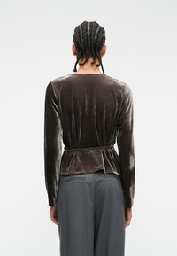 Top de catifea gri închis cu mâneci lungi, detalii cu fundiță la spate și design peplum, asortat cu pantaloni gri. Textură netedă și strălucire moale.