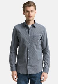 Gestreiftes Hemd aus marineblauem und grauem Stoff mit einer Brusttasche und einem klassischen Kragen, kombiniert mit Jeans.