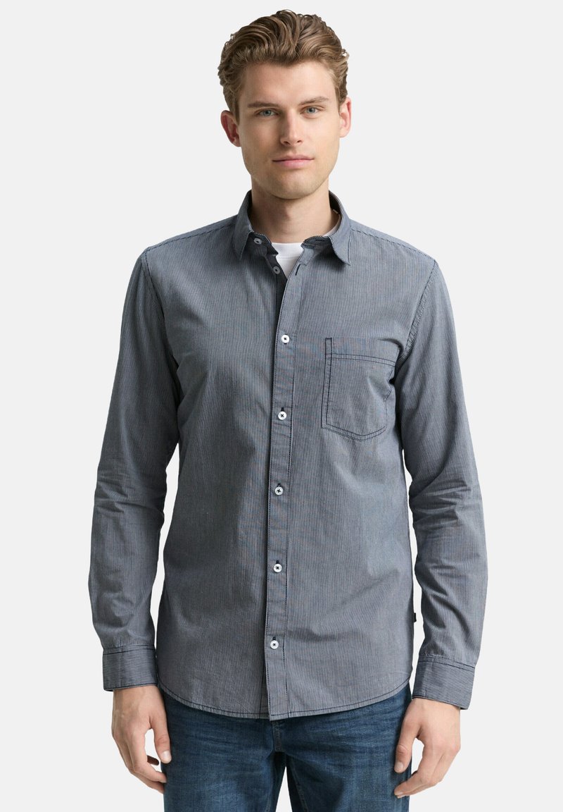 Gestreiftes Hemd aus marineblauem und grauem Stoff mit einer Brusttasche und einem klassischen Kragen, kombiniert mit Jeans.