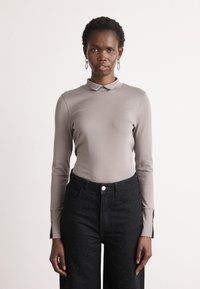 Haut ajusté à manches longues en gris clair avec un col. Associé à un jean noir taille haute avec des embellissements à pois et des fentes latérales.