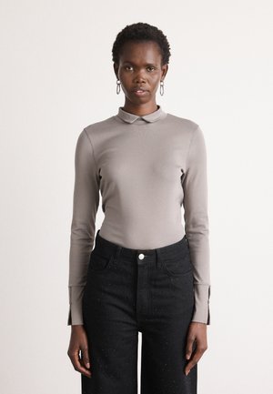 Lange mouw, aansluitend shirt in lichtgrijs met een kraag. Gecombineerd met hoge zwarte jeans met stippenversieringen en zijsplitten.