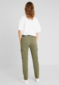 Oliwkowe spodnie cargo o dopasowanym kroju, z bocznymi kieszeniami i szlufkami na pasek, zestawione z luźną białą koszulką.