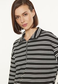Top con zip a righe bianche e nere, con colletto e texture a coste. Presenta righe orizzontali e chiusura con zip al collo.