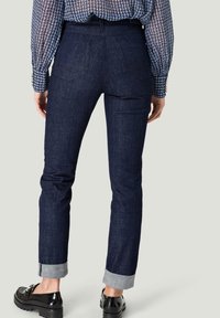 Mörkblå denimjeans med rak passform, uppvikta benslut och två bakfickor. Kombineras med svarta lackskor och en mönstrad långärmad topp.