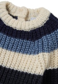 Primo piano di un colletto di maglione lavorato a maglia con una spessa trama a coste, in crema, blu navy e strisce orizzontali blu.