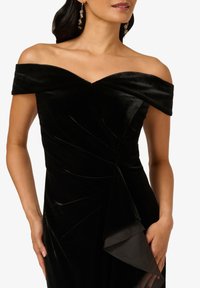 Zwarte fluwelen off-shoulder jurk met een aansluitende lijfje, gedrapeerde details en een gelaagde chiffon zoomaccent. Elegante stijl met een gladde textuur.