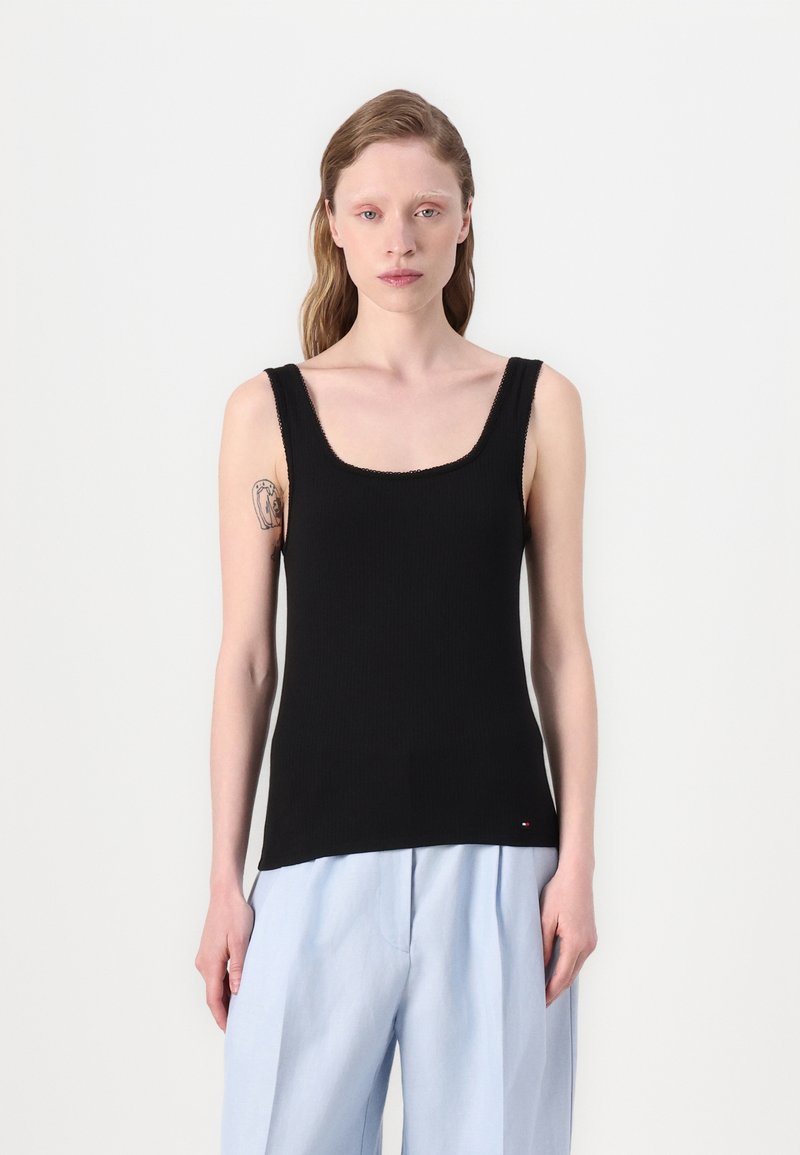 Fekete, bordázott, négyzet alakú nyakú tank top széles pántokkal, világoskék, laza szabású nadrággal párosítva. Jelentős varrási részletek.