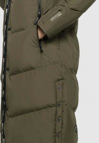 Giacca a vento verde oliva lunga con design trapuntato, chiusura con zip frontale e dettagli neri. Presenta un logo sulla manica e bottoni a pressione.