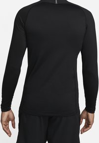 Rückansicht einer Person, die ein passendes schwarzes Langarm-Sportshirt und schwarze Hosen vor einem schlichten Hintergrund trägt.