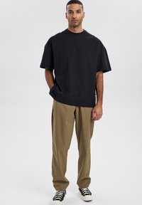 Sort oversized bomulds t-shirt med rund hals, parret med khaki løstsiddende bukser og sorte sneakers med hvide såler.
