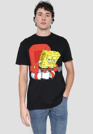 Schwarzes T-Shirt mit einem Grafikdesign von SpongeBob Schwammkopf auf einem roten Stuhl, mit einem verspielten Ausdruck und hellgelben Akzenten.