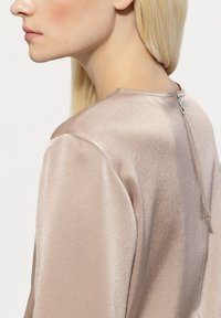 Satin blouse in light taupe with a round neckline, short sleeves, and a back zip closure. Smooth texture, minimalistic design.