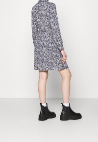 Abito a fantasia floreale in blu navy con colletto alto e maniche lunghe, abbinato a stivali neri in pelle alla caviglia e calzini bianchi.