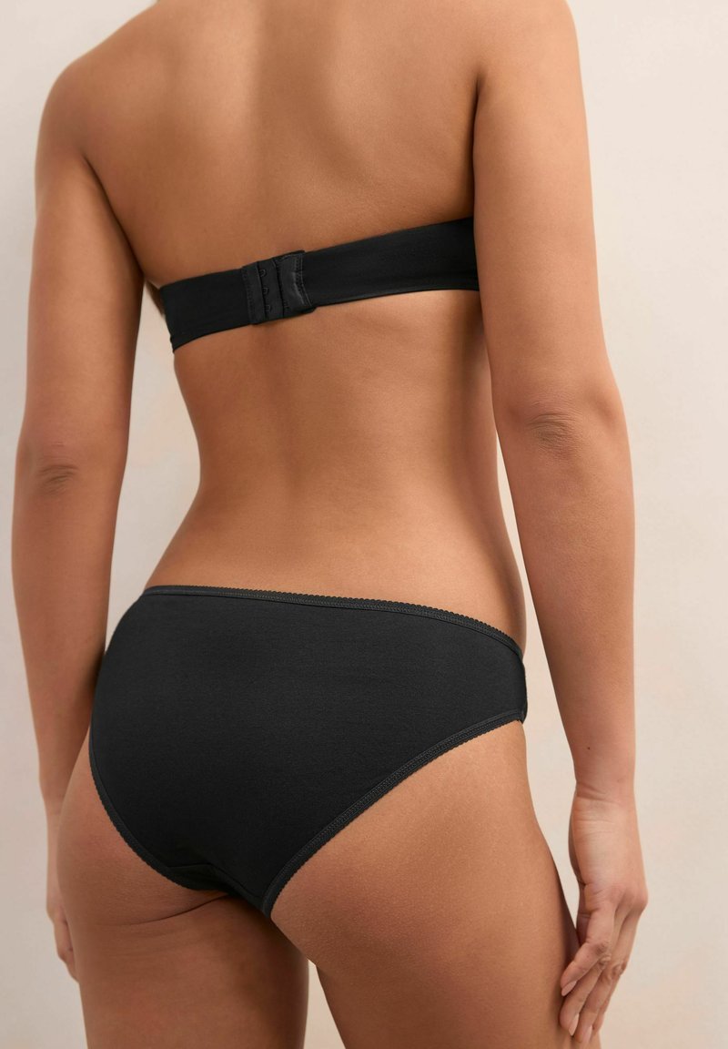Černá bandeau podprsenka a odpovídající bikiny, vyrobené z hladkého materiálu, s jemně vlnkovanými okraji a zapínáním na háček na zadní straně.