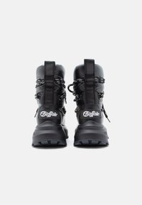 Pár černých zateplených zimních bot značky Buffalo s silnými podrážkami a vzorovanými tkaničkami, pohled zezadu na bílém pozadí.