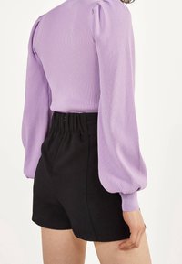 Top in lavanda a coste con maniche lunghe a sbuffo abbinato a pantaloni corti neri a vita alta con una cintura elastica per il massimo comfort.