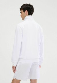 Sudadera blanca con cuello alto, mangas largas y puños de canalé. Textura suave, diseño minimalista sin patrones ni acentos.