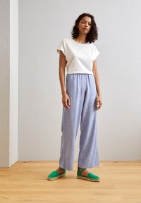 Vit t-shirt med kort ärm, ljusblå vida byxor och gröna espadrillos. Enkelt mönster med en avslappnad passform och mjuk textur.