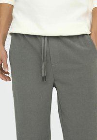 Gray ribbed pants with a relaxed fit, featuring a drawstring waist and side pockets. Textured fabric with subtle vertical lines.