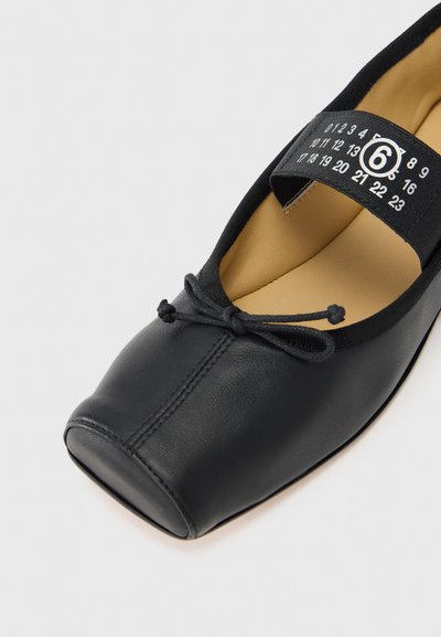 Μαύρο δερμάτινο μπαλαρίνα με στρογγυλερή μύτη, διακοσμητικό λεπτομέρεια κόμπου και ελαστικό λουράκι με σημάνσεις μεγέθους σε μαύρη ετικέτα.