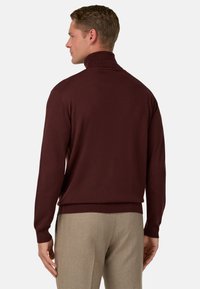 Bordo krāsu augstvērtīgā turtlenecka džemperis ar ribotu apkakli un aprocēm, izgatavots no gludas adījuma auduma; kopā ar gaiši pelēkiem piegrieztiem biksēm.