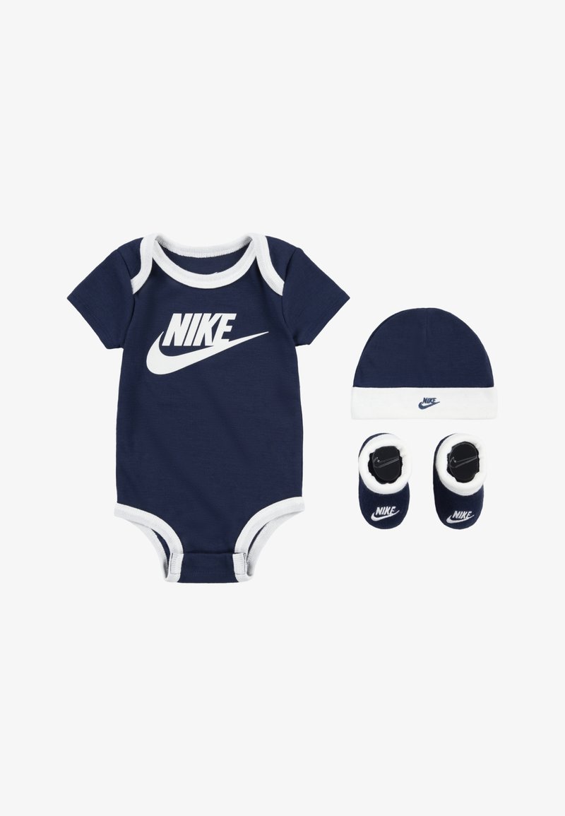 Sötétkék pamut rugdalózó fehér díszítéssel és nagy Nike logóval, amelyhez egy összeillő sapka és cipőcske tartozik, mindkettőn a Nike logóval.