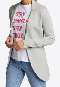 Lichtgrijze cardigan met een op maat gemaakt ontwerp. Zachte stof, open voorkant, lange mouwen, gecombineerd met een wit t-shirt met roze tekst.