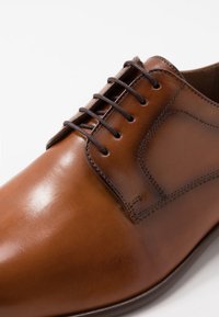 Brown leather dress shoe with a smooth finish, featuring a stitched side panel and dark brown laces. Rounded toe and sleek silhouette.