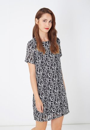 Vestido negro de manga corta con un patrón circular blanco, tela ligera, ajuste ligeramente holgado, largo hasta la rodilla y escote redondo.