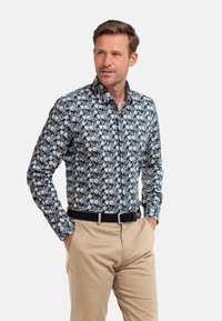 Heren overhemd met knopen in donkere blauwe stof met wit en roze bloemenpatroon. Lange mouwen, kraag, gecombineerd met beige broek en zwarte riem.