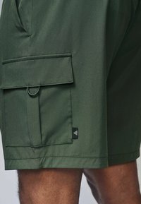 Grønne cargo shorts lavet af glat stof, med en sidelomme, løbdetalje og et lille mærkat på kanten.