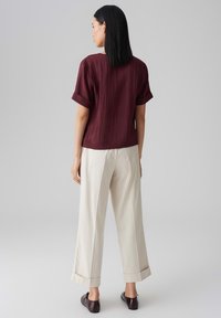 Burgunderfarbendes Kurzarmoberteil mit umgeschlagenen Ärmeln, kombiniert mit cremefarbenen weiten Hosen. Der Look zeichnet sich durch eine lässige Silhouette und eine weiche Textur aus.