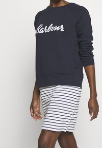 Námořnická mikina se bílým nápisem "Barbour", kulatým výstřihem a žebrovanými manžetami, spojená s pruhovanou sukní v bílé a námořnické barvě.