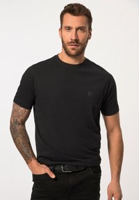 Svart bomull t-shirt med rundad halsringning, korta ärmar och en subtil logodesign på bröstet; bärs med svarta jeans och ett bälte.