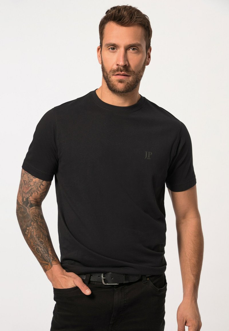 Svart bomull t-shirt med rundad halsringning, korta ärmar och en subtil logodesign på bröstet; bärs med svarta jeans och ett bälte.