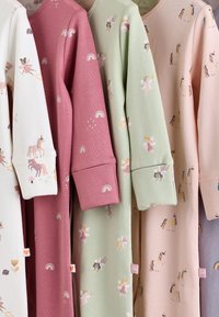 Quatre vêtements de nuit pour enfants sont suspendus côte à côte, fabriqués en coton aux couleurs pastel. Les motifs incluent des licornes, des fées et des arcs-en-ciel.