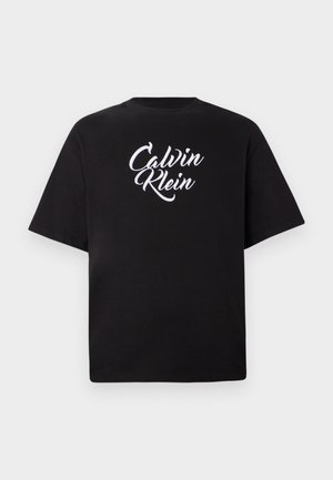 Czarna koszulka z krótkim rękawem z białym, kursywnym logo "Calvin Klein" umieszczonym na środku klatki piersiowej, wyeksponowana na jednolitym jasnym tle.