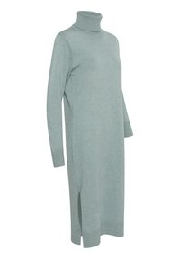 Gaiši zaļš turtlenecks kleita, izgatavota no mīksta adīta auduma, ar garām piedurknēm un sānu šķērsojumiem, lai nodrošinātu brīvību kustībā.