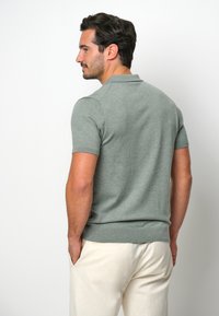 Grå kortärmad polo med ribbad nederkant och krage, tillverkad av mjukt trikåmaterial. Slät struktur med minimala designdetaljer.