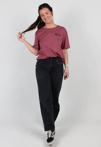 T-shirt marron à manches courtes avec un logo noir sur la poitrine, associé à un jean noir taille haute et des baskets noires.