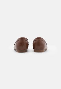 Mocasines de cuero marrón con una textura suave, punta redondeada, tacón bajo y un detalle de costura mínima en la parte trasera.