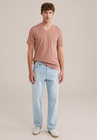 Világos rózsaszín V-kivágású póló világos kék egyenes szabású farmernadrággal és zöld részletekkel ellátott fehér sportcipőkkel párosítva. Sima szövet textura, laza megjelenés.