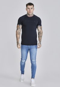 Marineblauw T-shirt met korte mouwen en bloemenaccenten bij de mouwen, gecombineerd met versleten lichtblauwe skinny jeans en witte sneakers.