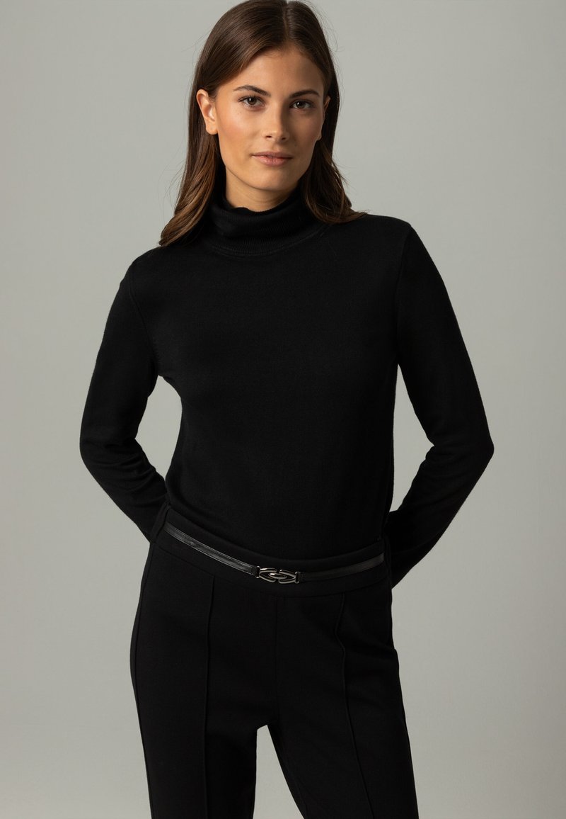 Schwarzer Rollkragensweater aus weichem Material, kombiniert mit maßgeschneiderten schwarzen Hosen. Der Gürtel hat eine elegante silberne Hardware-Akzentuierung.