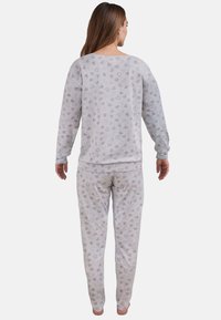 Vaaleanharmaa pyjamansetti, jossa on pehmeä tekstuuri. Settiin kuuluu pitkähihaista yläosaa ja elastisella vyötäröllä varustettuja housuja, jotka on koristeltu hillityillä sydänkuvioilla.