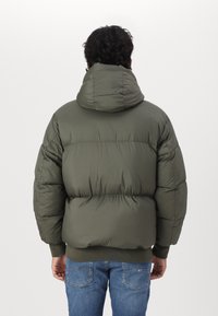 Chaqueta tipo puffer con capucha en verde oliva, con textura acolchada, puños y dobladillo acanalados, y un ajuste relajado. Diseñada para la calidez y la comodidad.