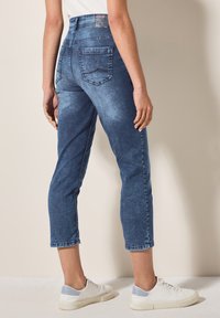 Jean cropped en denim bleu clair avec une taille haute, des poches arrière bien visibles et des ourlets retroussés, accompagnés de baskets blanches.